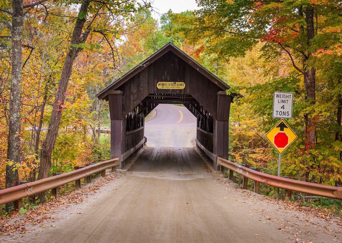 Ponte coperto del Vermont con fogliame autunnale sulla strada secondaria