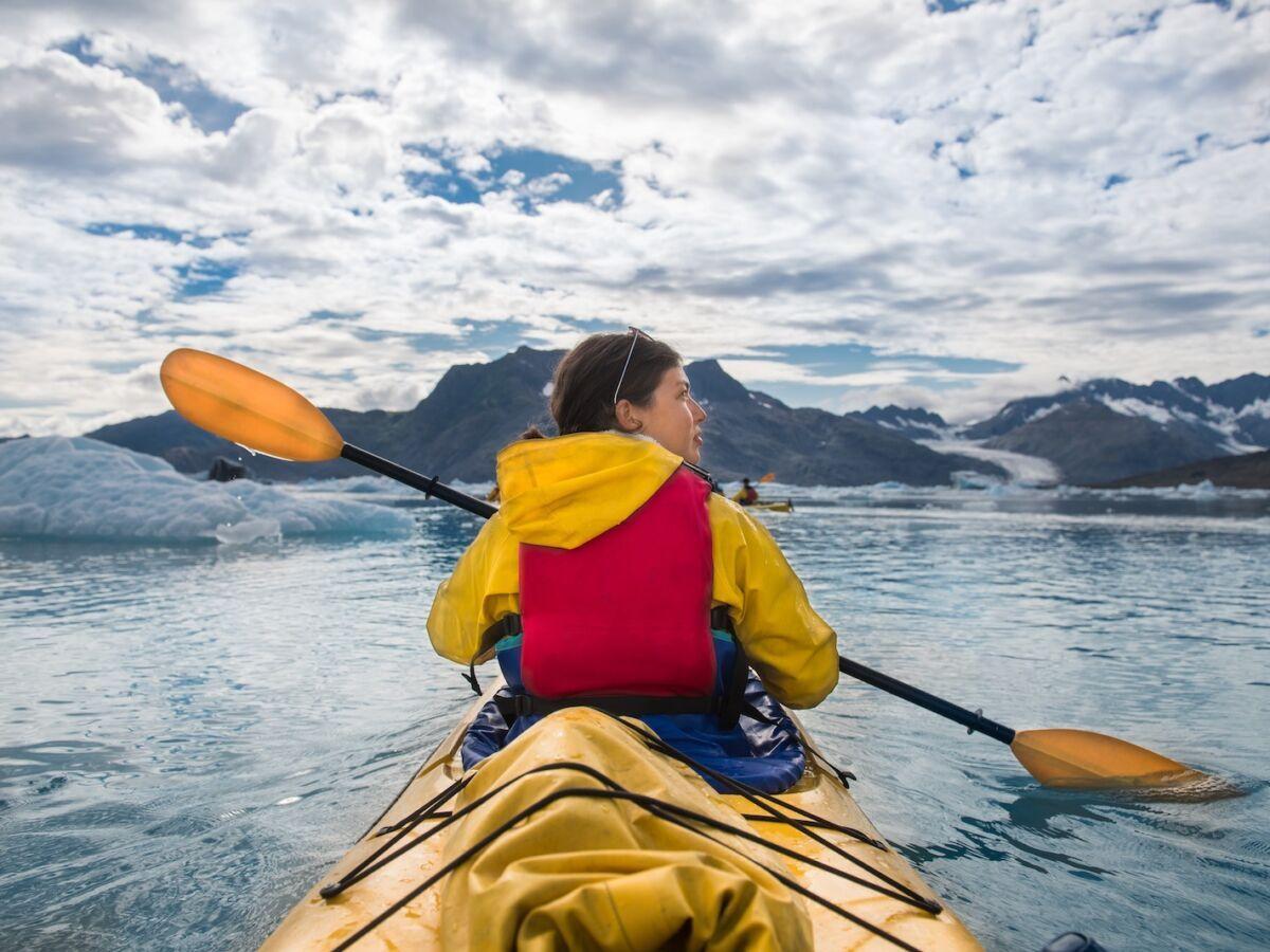 Donna che pagaia su una canoa in una baia ghiacciata in Alaska esplorando i ghiacciai
